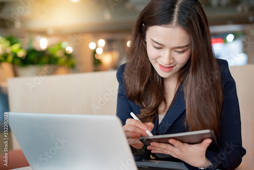 Working woman concept. Attractive young Asian businesswoman using digital tablet and computer working in modern office. Confident Female entrepreneur smiling at workplace. Work smart with technology.