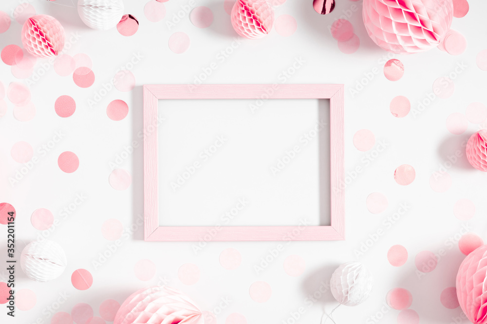 Festive white background with pink confetti, photo frame, paper decoration. Holiday concept on white background. Birthday, wedding, party. Flat lay, top view, copy space