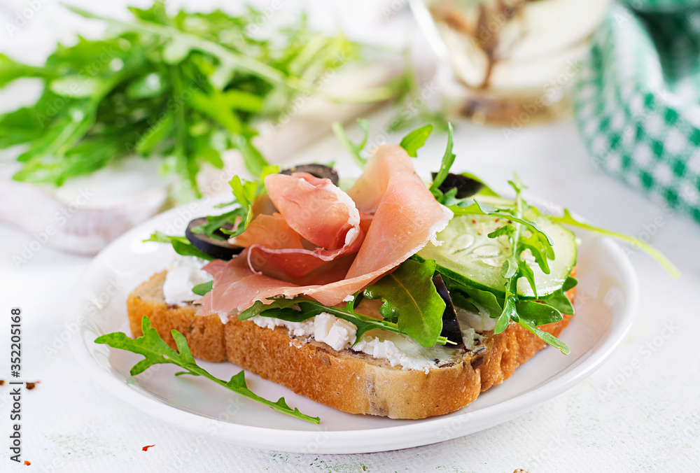 Sandwich with prosciutto, cucumber, black olives, arugula and feta cheese on  table.  Trend food.