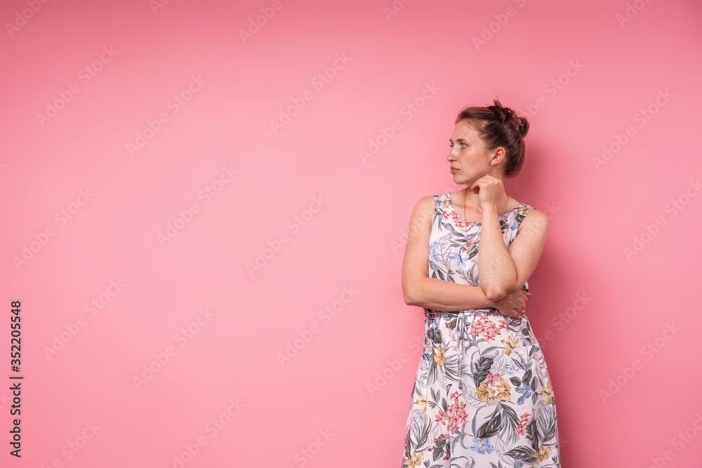 An attractive young woman in long dress with floral print, pink background. An attractive young woman in long dress with floral print, pink background.