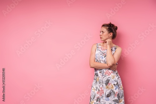An attractive young woman in long dress with floral print, pink background.