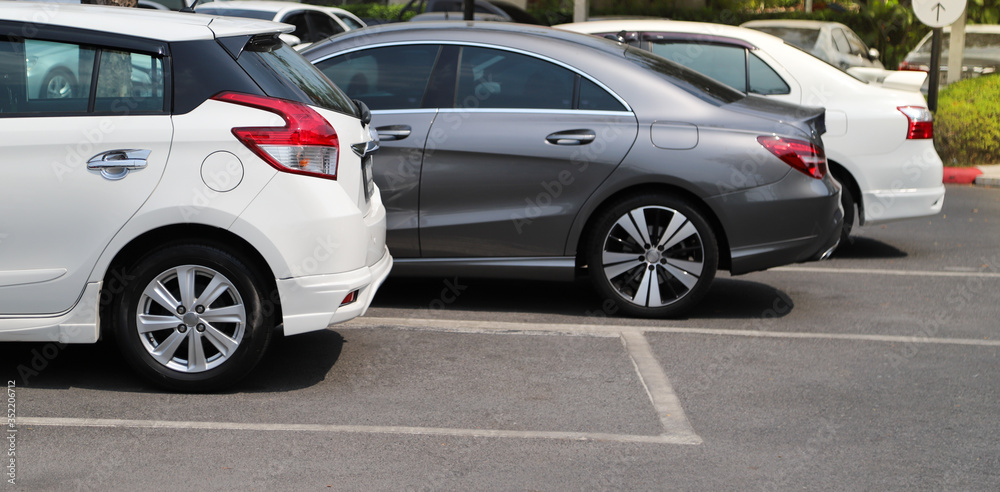 Closeup of rear, back side of white car with  other cars parking in outdoor parking area.