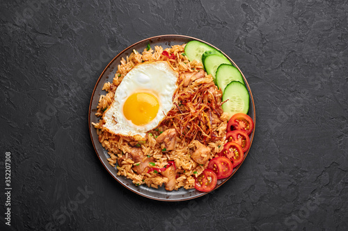 Nasi Goreng - Indonesian Chicken Fried Rice on black plate on dark slate backdrop. Nasi Goreng is an Indonesian cuisine dish. Balinese Food. Asian meal. Top view