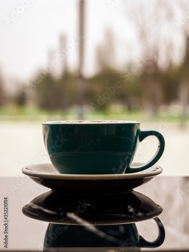 Mirror image of a beautiful stylish mug in the dark surface of the table. A Cup of hot coffee in a restaurant with copy space. Vertical image of a blue Cup and saucer in a public place