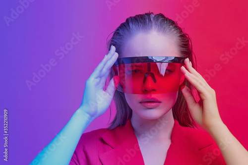 Cool stylish girl with a fashionable hairstyle and stylish glasses with a large glass poses on a bright neon background.
