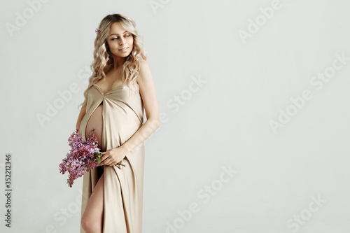 Pregnancy and motherhood concept - portrait of happy beautiful pregnant woman with lilac flowers in her hands on gray background, isolated