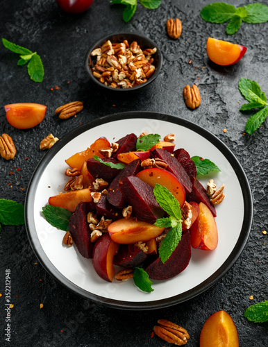 Vegan Plum, beet salad with pecan nuts, mint and herbs on rustic black table
