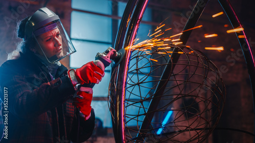 Young Contemporary Female Artist is Grinding Her Metal Tube Sculpture with a Handheld Power Tool in a Studio Workshop. Empowering Woman Makes Modern Brutal Abstract Artwork Out Of Metal.
