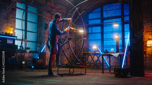 Handsome Male Artist Uses an Angle Grinder to Make Brutal Metal Sculpture in Studio. Hipster Guy Polishes Metal Tube with Sparks Flying Off It. Contemporary Fabricator Creating Abstract Steel Art.