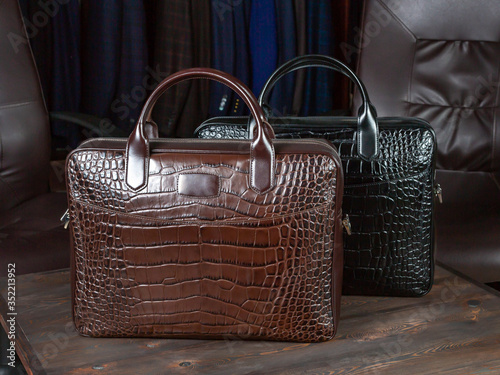 Two travel bags made of crocodile leather on the background of the assortment of men's clothing store