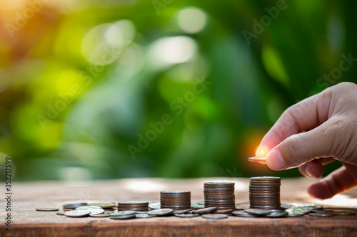 Coins in glass jar set on wooden plates, put in a green background