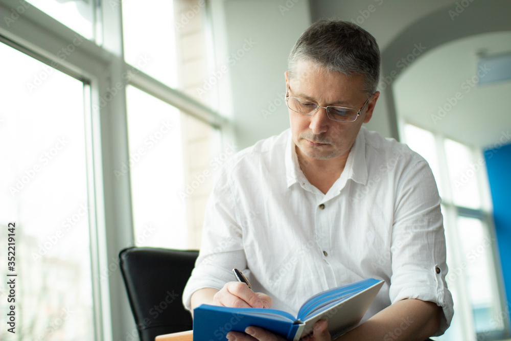 Fototapeta premium A man in a white shirt makes a note in a notebook.