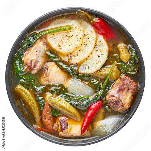 Sinigang na Baboy or Filipino Pork Meat Soup in black bowl isolated on white backdrop. Sinigang is a Filipino cuisine dish with meat, bamia, daikon, spinach, fish sauce. Filipino Food. Asian Meal photo