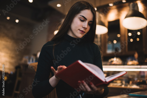 Focused young woman reading book in cafe