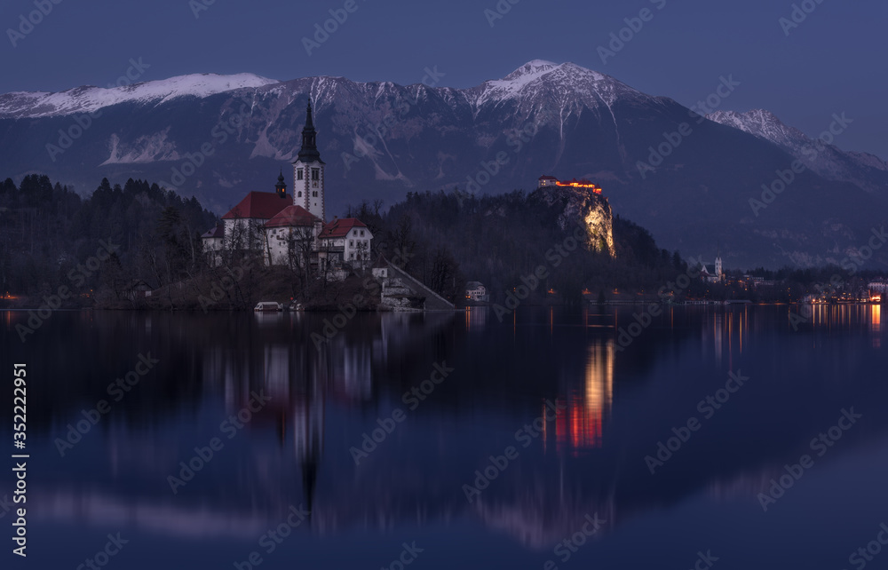 Church Of Mary The Queen, Also Known As The Pilgrimage Church Of  Assumption Of Mary, Or Our Lady Of The Lake Bled At Winter « Blue Hour » With Karavanke Mountain Range  And Parish Church Of St.Martin