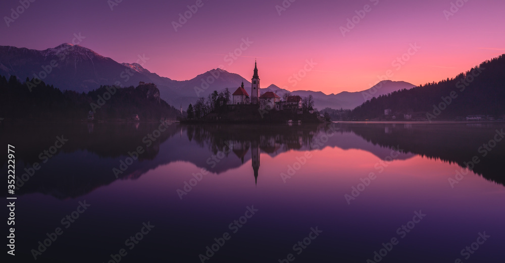 Tranquility Winter Rising Of The Sun At Lake Bled, Slovenia.Windless Reflection Church of Mary the Queen, Parish Church Of St.Martin And Smoke On The Water.Perfect Combination Architecture And Nature