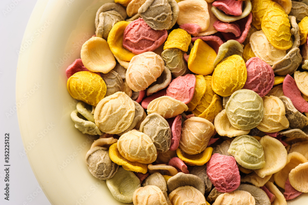 uncooked colored homemade pasta in a bowl close-up on a white table, top view uncooked colored homemade pasta in a bowl close-up on a white table, top view