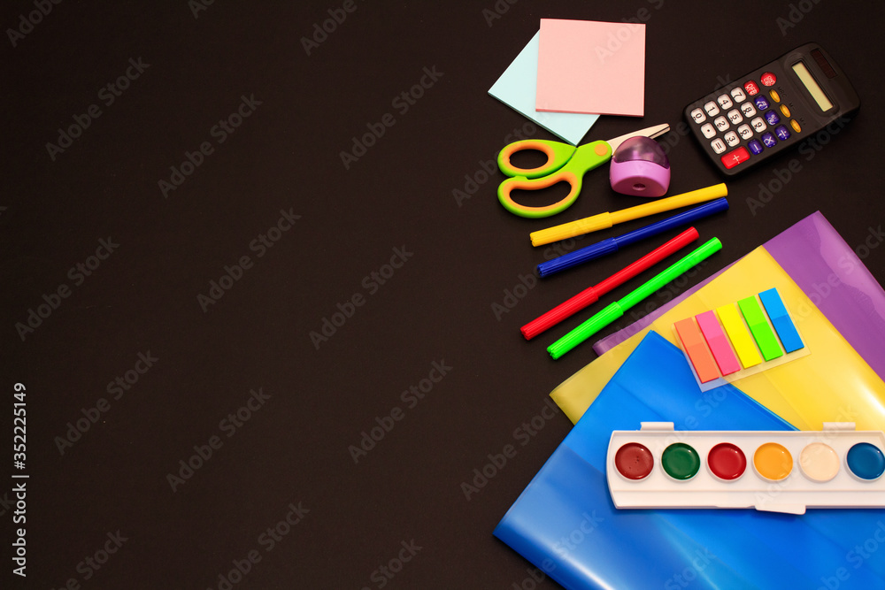 School accessories (pencils, pens, calculator, paper clips, paper, felt-tip pens, paints, scissors, textbook covers) on black paper background. School preparation concept School accessories (pencils, pens, calculator, paper clips, paper, felt-tip pens, paints, scissors, textbook covers) on black paper background. School preparation concept