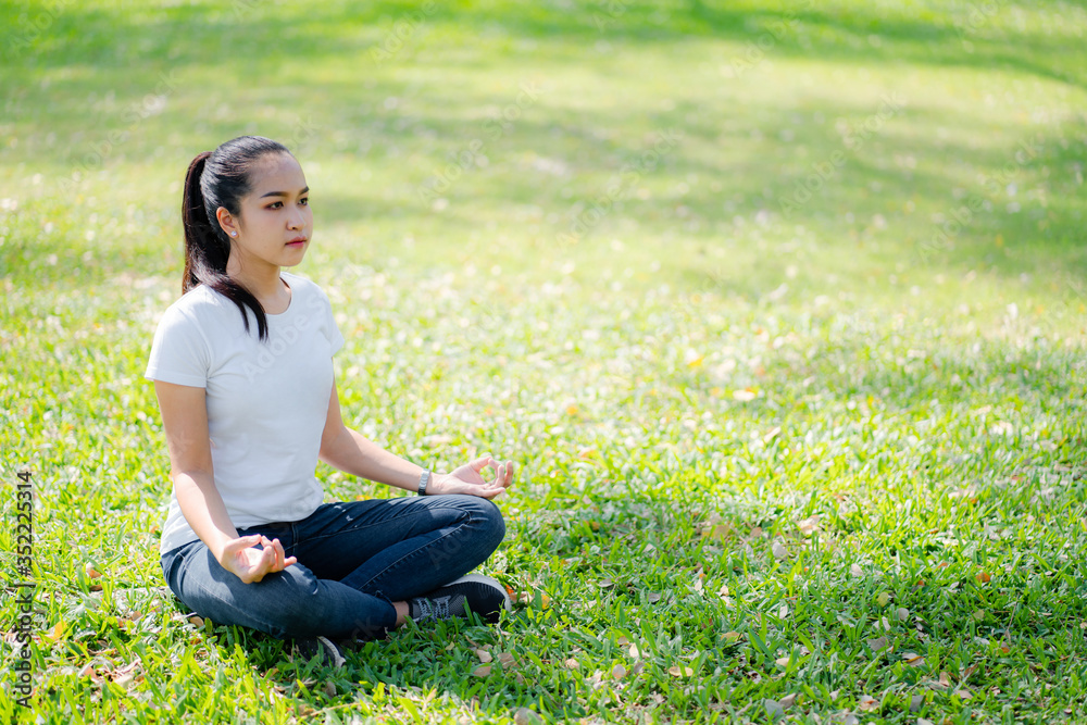 Asian young women meditation yoga with smile face for peace, relaxation emotional on green grass of park with natural light sunset of the sun with dramatic yellow and orange sky. Image depth of field. Asian young women meditation yoga with smile face for peace, relaxation emotional on green grass of park with natural light sunset of the sun with dramatic yellow and orange sky. Image depth of field.