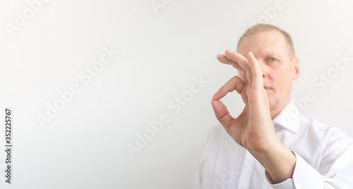 bright picture of male hand showing ok sign jesture in a white shirt on a white background. Blurred face. Copy space. banner. Everything will be OK concept photo