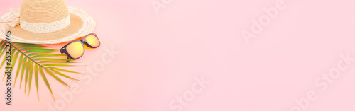 summer accessories concept from sunglasses, straw hat and palm leaf on pastel pink background, for banner advertising.