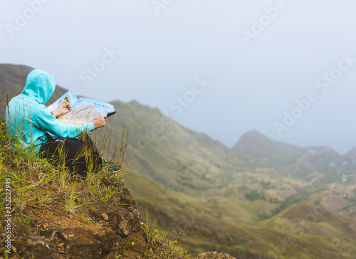 Traveler wear blue hoodie with the map sitting on the hill of a mountain in front of a gorgeous panorama view to the valley photo