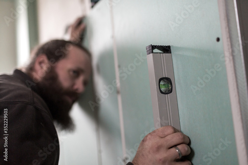 Hendwerker mit Bart prüft die Ausrichtung der Wände aus Gipsplatte mit einer Wasserwaage photo