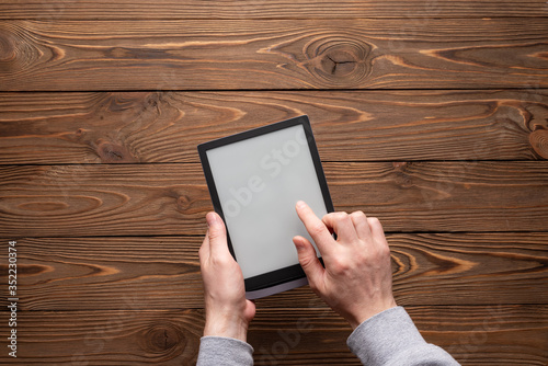 A modern black ebook with a white blank screen with male hand on a dark wooden background top view
