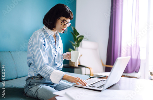 Beautiful woman working on a laptop at home. Attractive freelancer using laptop and drinking coffee. The girl chatting with friends in social network, shopping online, writing email.