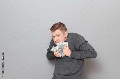 Fototapeta Portrait of funny unhappy greedy man clasping money to his chest