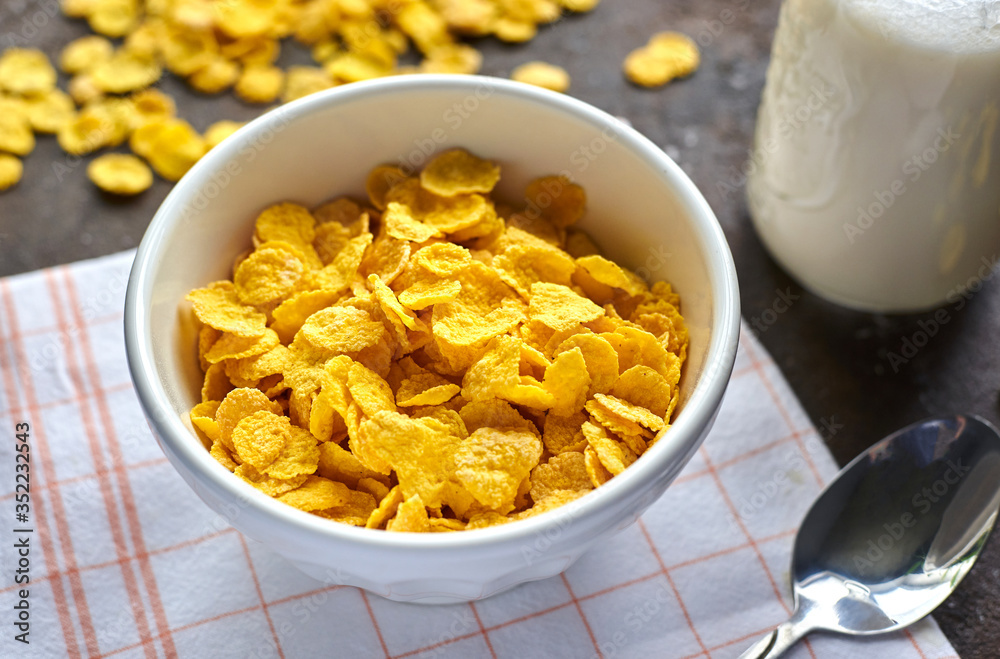 yellow cornflakes with milk in a white deep plate on a brown table yellow cornflakes with milk in a white deep plate on a brown table