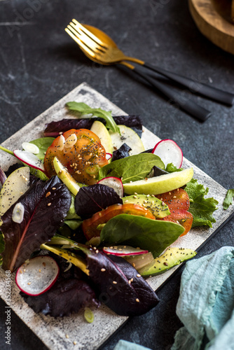 delicious tomato and guacamole lettuce salad, with green apple and radish on dark background