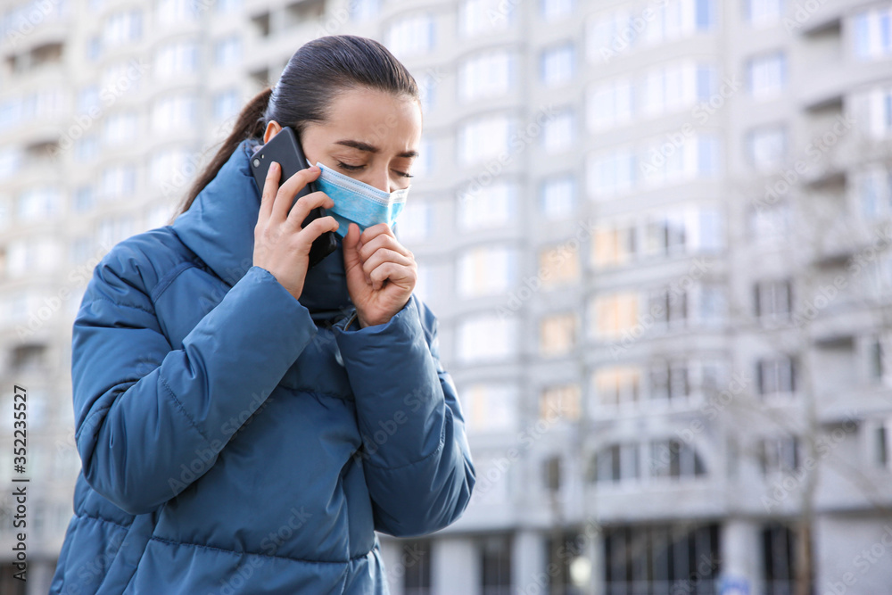 Woman with disposable mask talking on phone outdoors. Dangerous virus