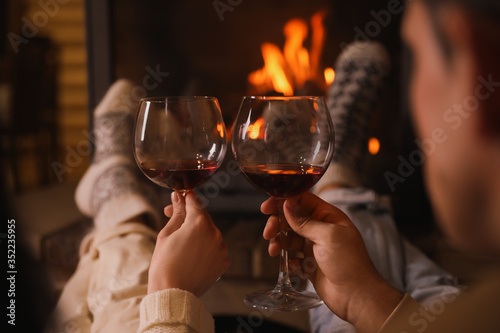 Bild auf Leinwand Couple with glasses of red wine near burning fireplace, closeup