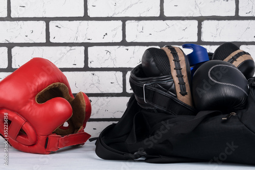 black sports bag with things for training and a red protective boxing helmet on a brick wall background