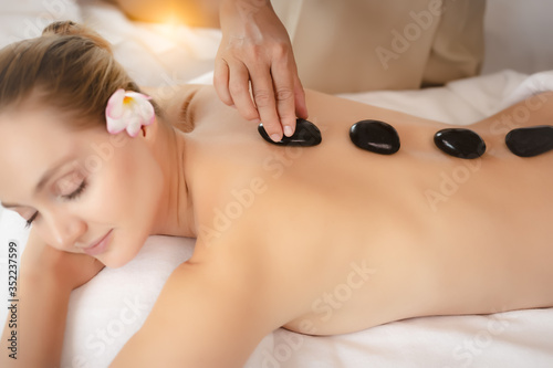 Professional beautician massaging female back by hot stones massage. Young woman getting hot stone massage in spa salon. Professional therapist masseuse putting hot stones massage to customer back