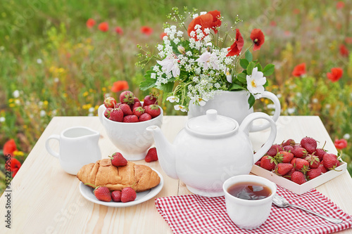 Romantic Valentines french or rural breakfast: tea, strawberries, croissants on table in poppy field. Countryside and Cozy Good morning weekend concept. Background with copy space. Date outdoors