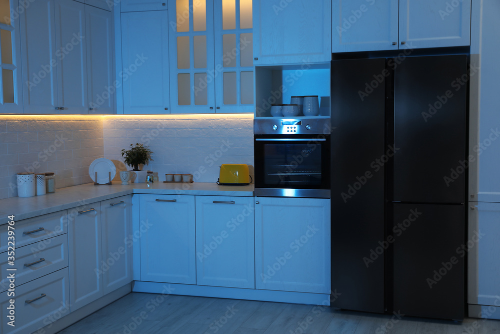 Fototapeta premium Stylish kitchen interior with modern refrigerator at night