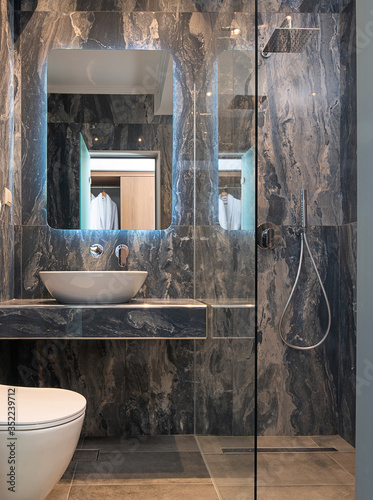 Front view of contemporary gray marble bathroom with vessel bowl sink, mirror back light, glass shower cabin, stone wall and floor