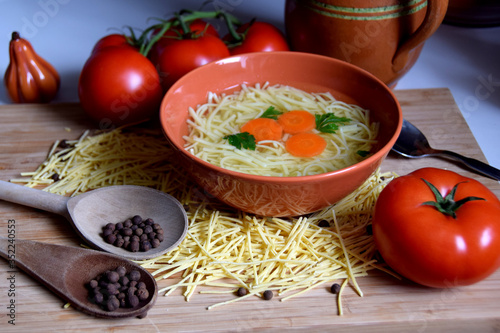 delicate chicken broth in a bowl next to tomatoes, spices and kitchen utensils