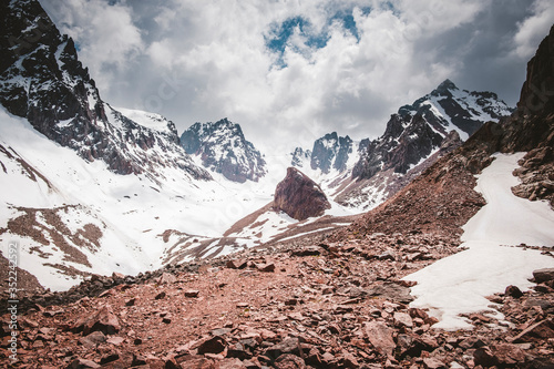 Panorama of the Trans Ili Alatau mountain range of the Tien Shan system in Kazakhstan near the city of Almaty. Rocky peaks covered with snow and glaciers in the middle of summer under clouds photo