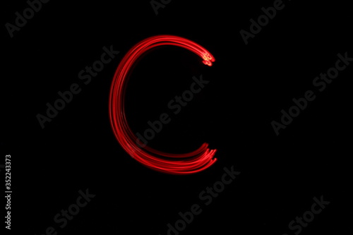 Long exposure photograph of the letter c in neon red colour fairy lights against a black background. Light painting photography. Part of an alphabet series. 