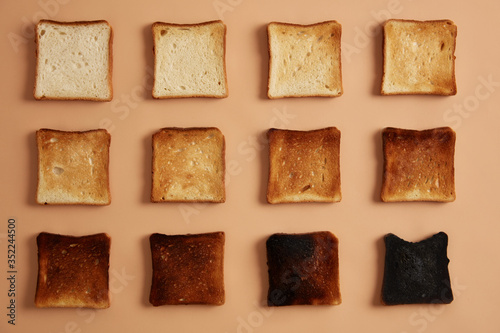 Slices of bread of various degree of toastiness arranged in rows against beige background. Toast or snack for eating. Stages of toasting. Healthy eating, munchies and dieting concept. Studio photo