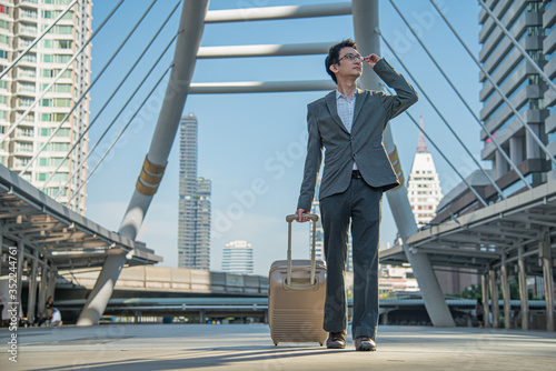 Young Businessman with eyeglasses carrying suitcase and hand holding eyeglass looking up for a future job, hope, direction and opportunity.