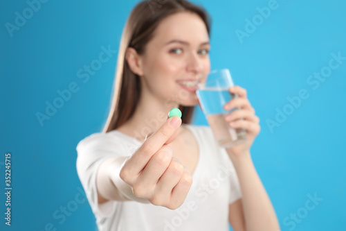 Young woman with glass of water and vitamin pill against blue background, focus on hand © New Africa