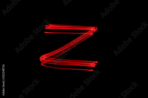 Long exposure photograph of the letter z in neon red colour fairy lights against a black background. Light painting photography. Part of an alphabet series. 