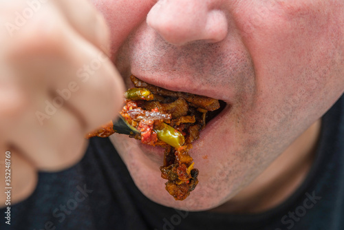 A man sends fried meat with sauce from a fork to his mouth, closeup. © andov