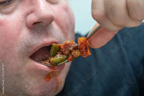 A hungry and fat fat man eagerly eats roasted meat with spices, fat from his mouth flows through his beard. © andov