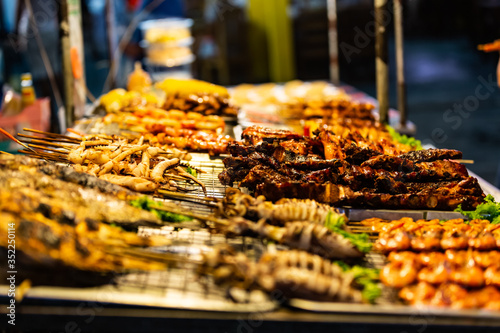 Differential focus of lateral close up view of street food market in the evening in Thailand. Typical Asian diverse fried food. Delicious shrimp, octopus, squid, fish, pork ribs are visible. photo