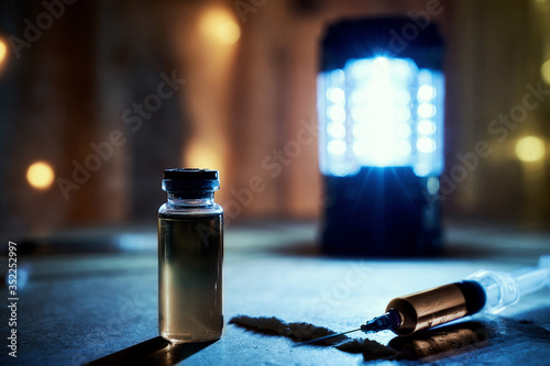 Bottle of heroin and narcotic syringes. In syringes and vials, the liquid is yellow, blue, and purple. cocaine and other drugs on old plywood in a dark room. Illuminated by cold and warm light.